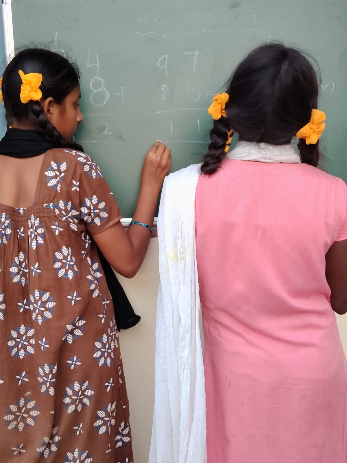 Two students working through an arithmetic problem on their new classroom blackboard